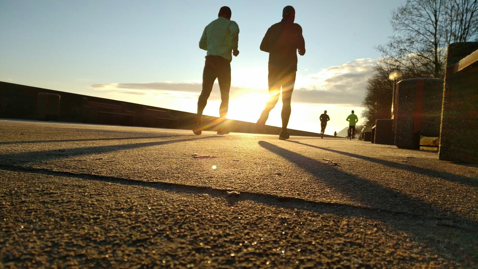Two runners in silhouette jogging on a paved path at golden sunrise